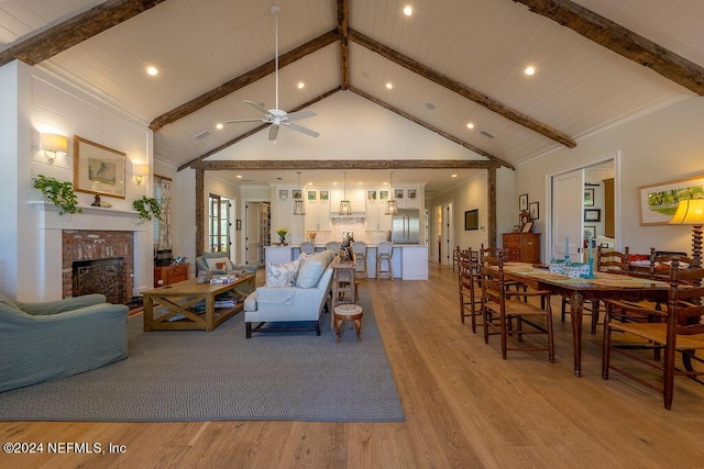 living room featuring beam ceiling, high vaulted ceiling, light wood-type flooring, ceiling fan, and a fireplace