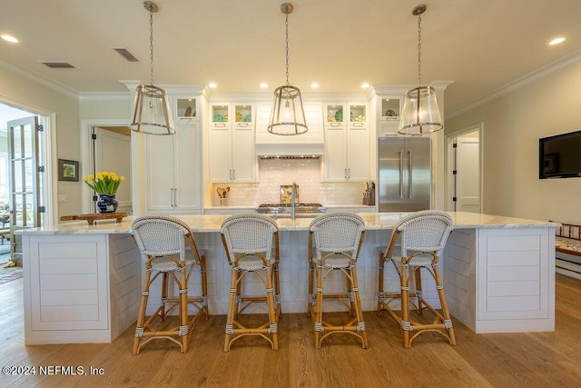 kitchen featuring built in fridge, light stone countertops, white cabinets, and a large island with sink