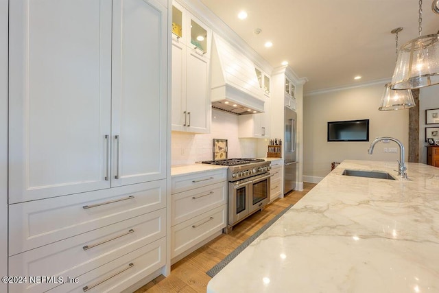 kitchen with sink, high end appliances, white cabinetry, light stone counters, and decorative light fixtures