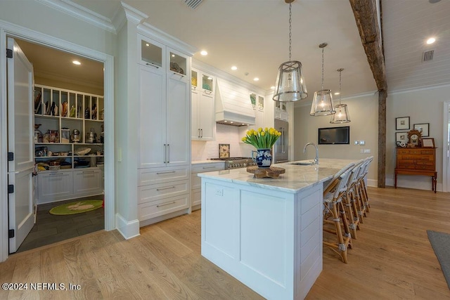 kitchen featuring sink, custom range hood, a center island with sink, and white cabinets