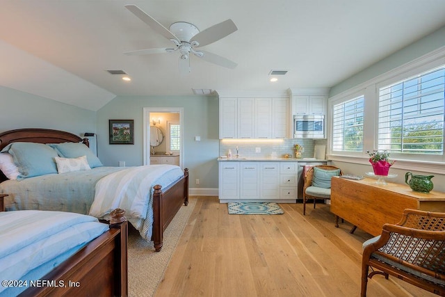 bedroom featuring ceiling fan, vaulted ceiling, ensuite bath, and light wood-type flooring