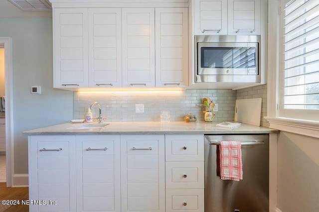 kitchen with sink, white cabinetry, light stone counters, appliances with stainless steel finishes, and decorative backsplash