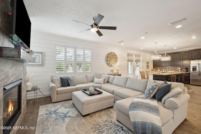 living room with a textured ceiling, sink, a tile fireplace, and light wood-type flooring