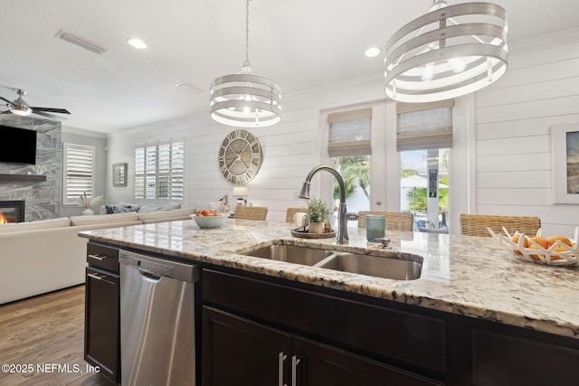 kitchen featuring sink, dishwasher, ornamental molding, a large fireplace, and light stone countertops