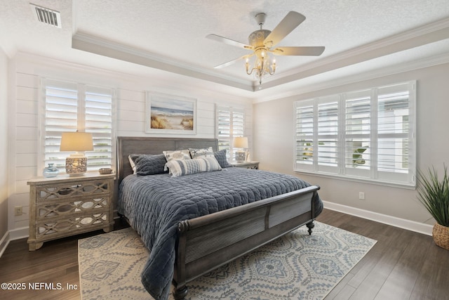 bedroom featuring dark hardwood / wood-style flooring, ornamental molding, a raised ceiling, and a textured ceiling