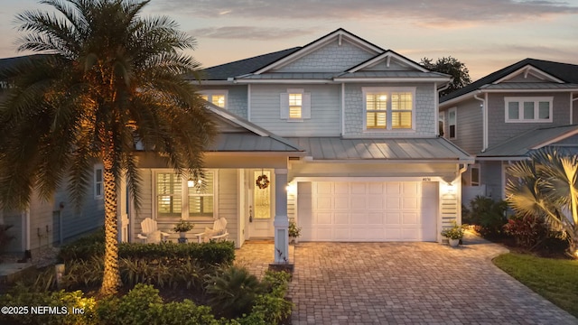 view of front of home featuring a porch, a standing seam roof, decorative driveway, metal roof, and an attached garage