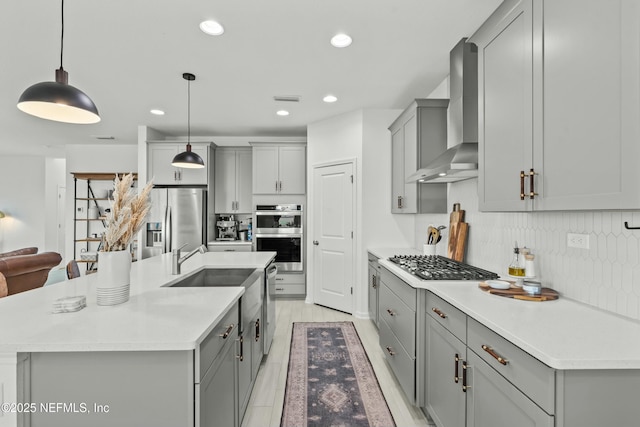 kitchen featuring hanging light fixtures, wall chimney exhaust hood, appliances with stainless steel finishes, and light countertops