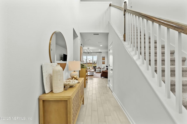 interior space with a notable chandelier, wood finish floors, visible vents, baseboards, and stairs