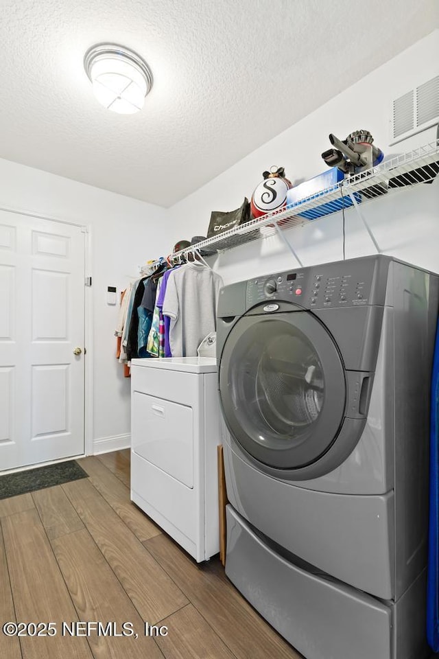 laundry room featuring hardwood / wood-style flooring, washing machine and dryer, and a textured ceiling