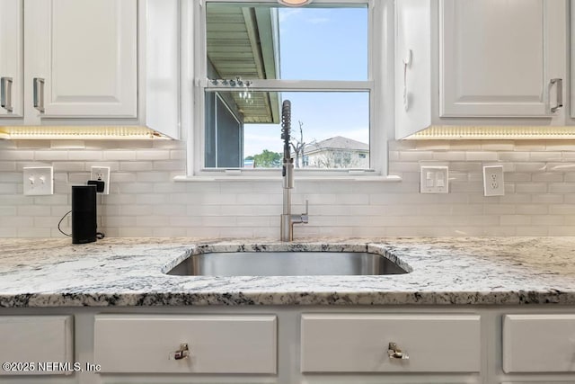 kitchen with white cabinetry, light stone countertops, sink, and backsplash