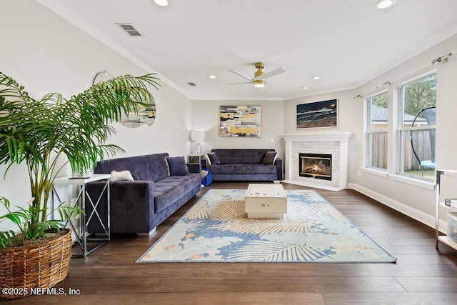 living room featuring a brick fireplace, crown molding, dark wood-type flooring, and ceiling fan