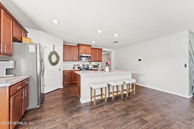 kitchen with a breakfast bar, appliances with stainless steel finishes, dark hardwood / wood-style floors, a textured ceiling, and a center island with sink