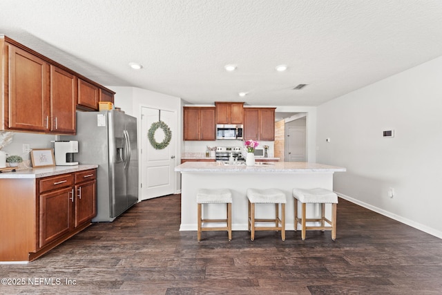 kitchen with a kitchen island with sink, dark wood-type flooring, a breakfast bar area, and appliances with stainless steel finishes