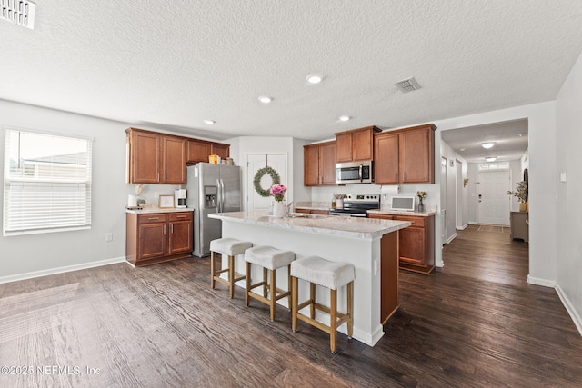 kitchen with sink, a breakfast bar area, appliances with stainless steel finishes, dark hardwood / wood-style floors, and a center island with sink