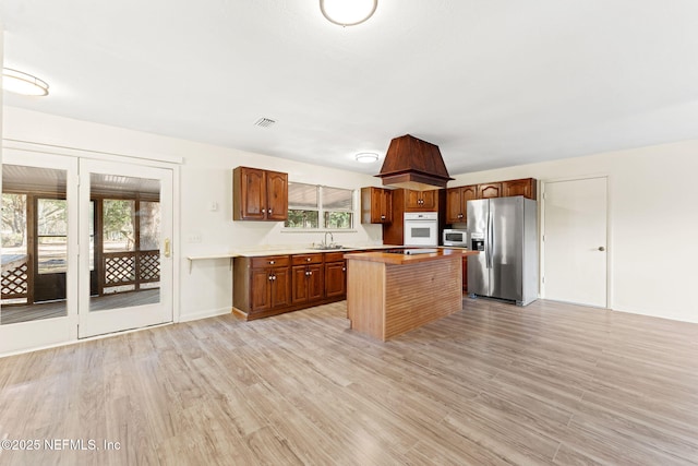 kitchen featuring light wood finished floors, a sink, light countertops, appliances with stainless steel finishes, and a center island