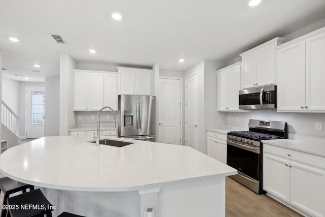 kitchen with light wood finished floors, stainless steel appliances, white cabinets, a sink, and an island with sink