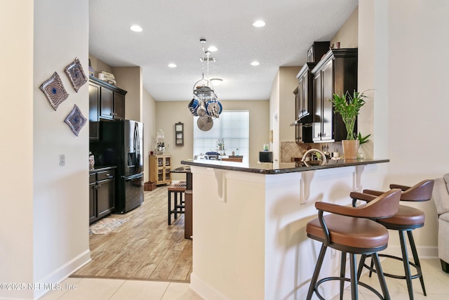 kitchen with a breakfast bar area, dark brown cabinetry, a peninsula, black refrigerator with ice dispenser, and dark countertops