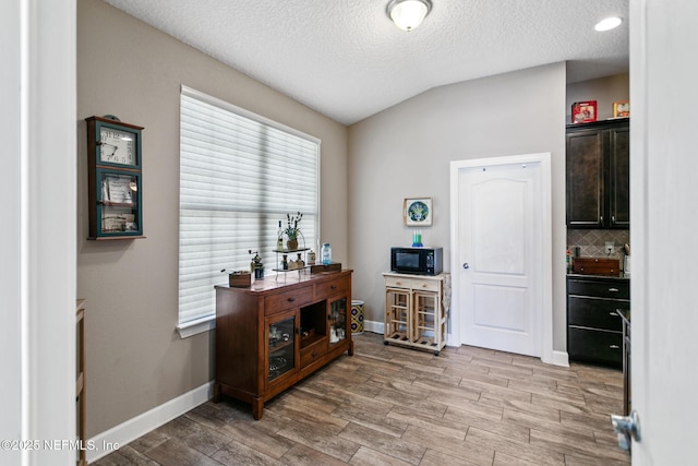 bar featuring black microwave, wood finished floors, baseboards, vaulted ceiling, and decorative backsplash