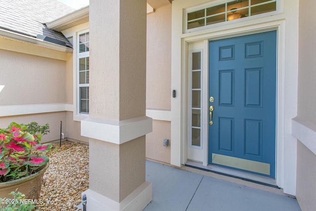 property entrance with stucco siding and roof with shingles