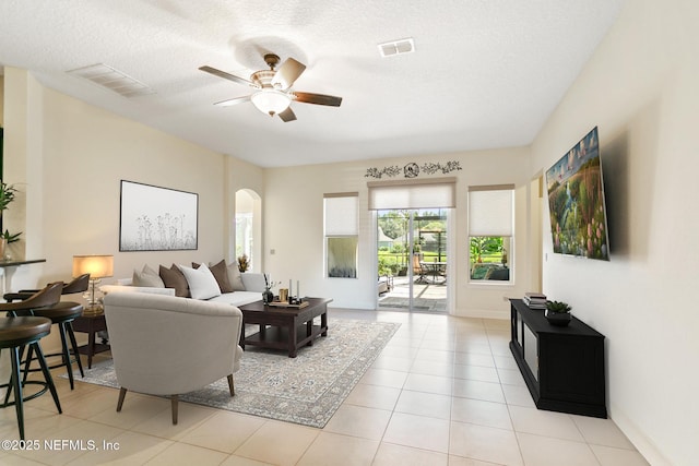 living room featuring light tile patterned floors, a textured ceiling, arched walkways, and visible vents