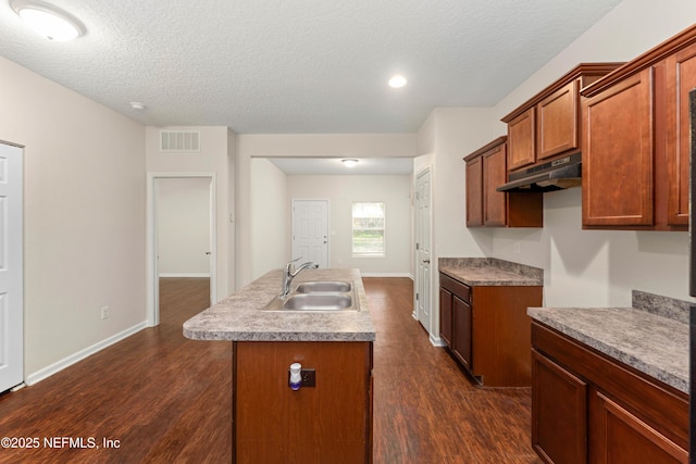 kitchen with an island with sink, sink, dark wood-type flooring, and a textured ceiling