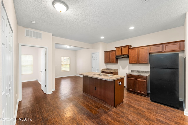 kitchen with sink, dark hardwood / wood-style flooring, a kitchen island with sink, black fridge, and a textured ceiling