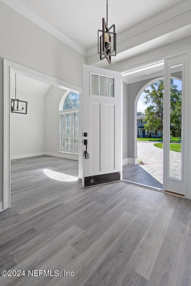 entryway featuring an inviting chandelier, ornamental molding, wood-type flooring, and a textured ceiling