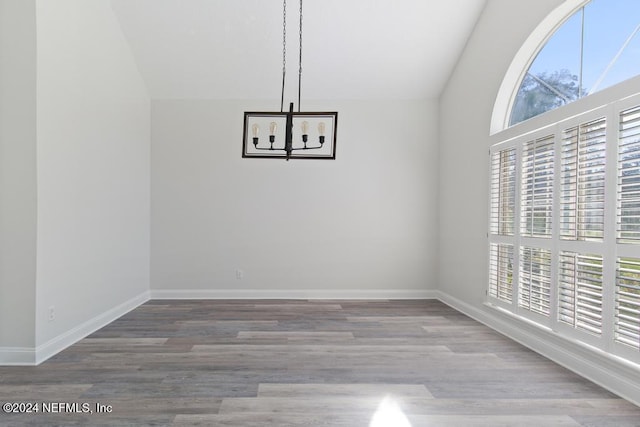 unfurnished dining area featuring plenty of natural light, vaulted ceiling, hardwood / wood-style floors, and a notable chandelier