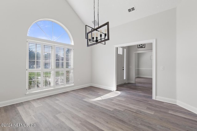 unfurnished dining area featuring hardwood / wood-style flooring, a towering ceiling, and an inviting chandelier