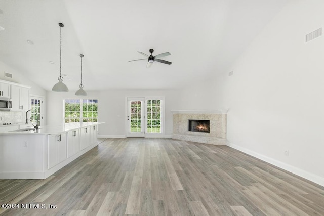 unfurnished living room with high vaulted ceiling, a fireplace, sink, ceiling fan, and light hardwood / wood-style floors