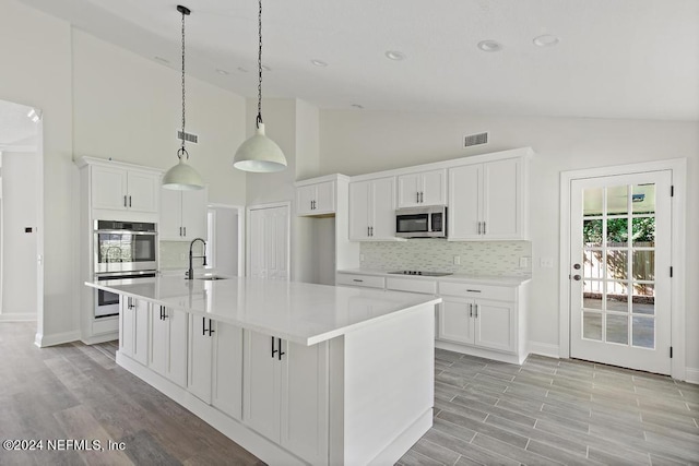 kitchen with hanging light fixtures, white cabinetry, appliances with stainless steel finishes, and a center island with sink