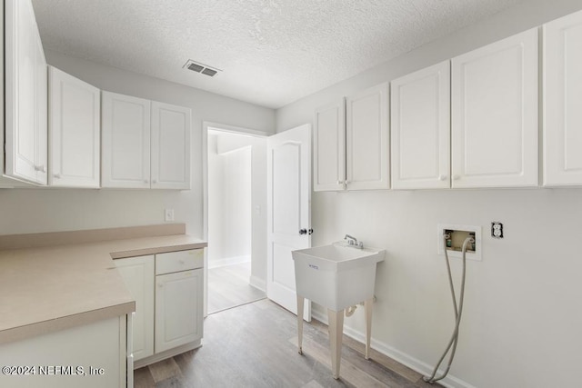 laundry area featuring cabinets, washer hookup, a textured ceiling, and light hardwood / wood-style flooring