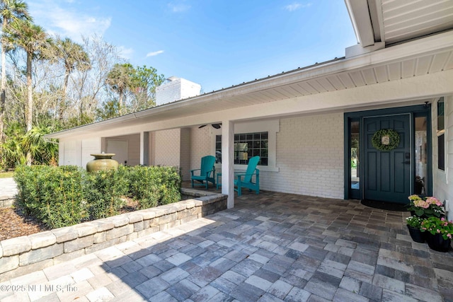 view of exterior entry featuring brick siding, a chimney, and a patio area