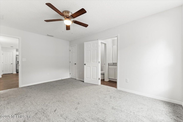 unfurnished bedroom featuring ceiling fan, ensuite bath, a textured ceiling, and dark colored carpet