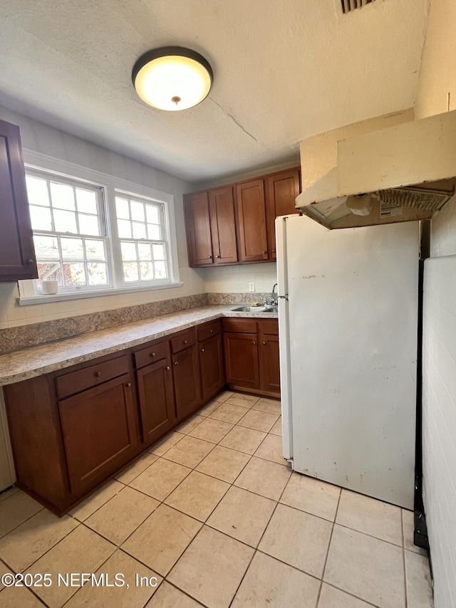 kitchen with white fridge, light tile patterned floors, and a textured ceiling