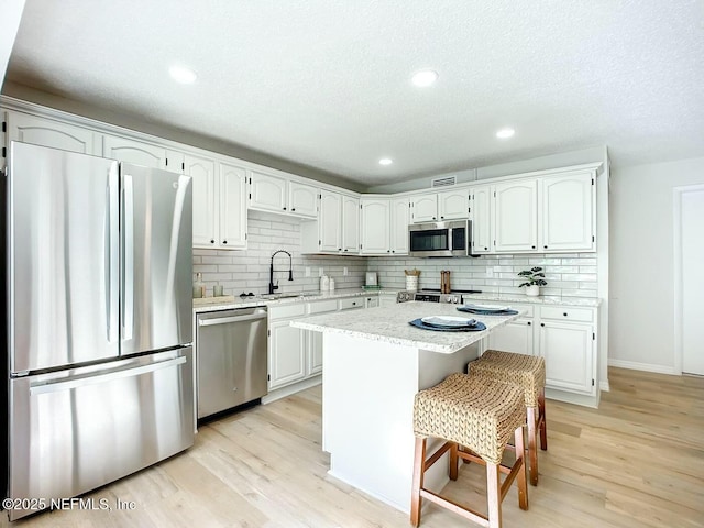 kitchen with appliances with stainless steel finishes, sink, a center island, light hardwood / wood-style floors, and white cabinets