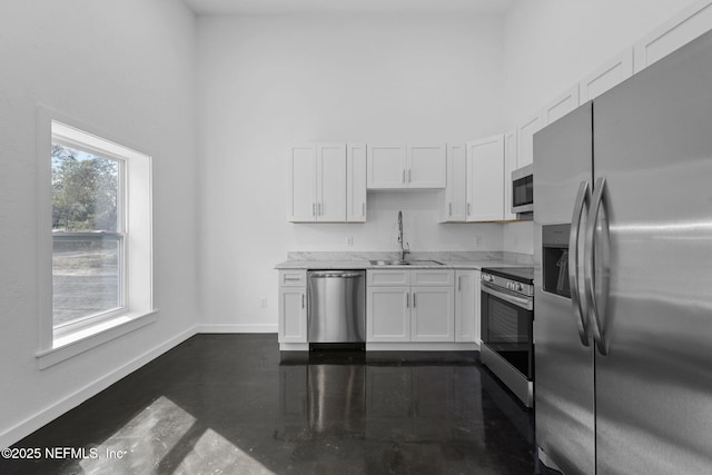 kitchen with sink, white cabinetry, light stone counters, appliances with stainless steel finishes, and a towering ceiling