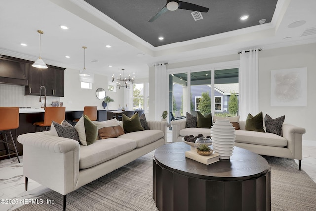 living room with a raised ceiling, ornamental molding, and ceiling fan with notable chandelier