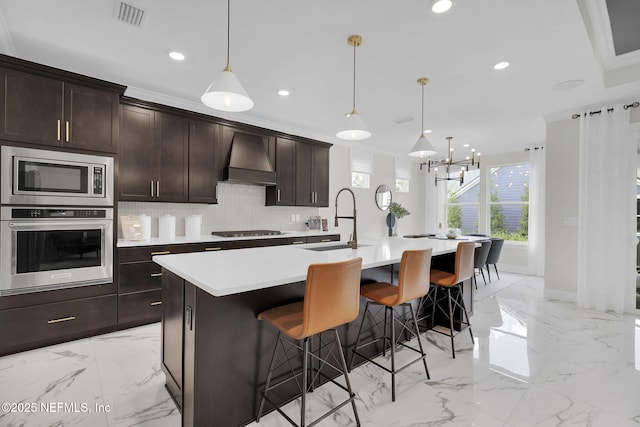 kitchen with stainless steel appliances, pendant lighting, custom range hood, and a center island with sink