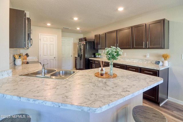 kitchen with dark brown cabinetry, sink, black refrigerator with ice dispenser, and kitchen peninsula