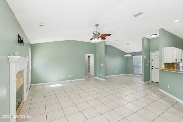 unfurnished living room featuring lofted ceiling, sink, a fireplace, light tile patterned flooring, and ceiling fan with notable chandelier