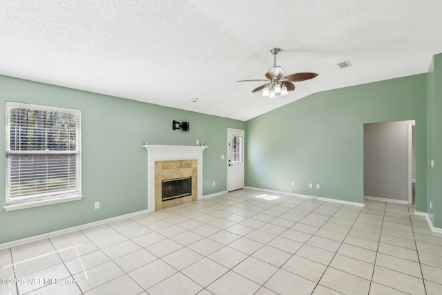 unfurnished living room with light tile patterned flooring, vaulted ceiling, a textured ceiling, ceiling fan, and a fireplace