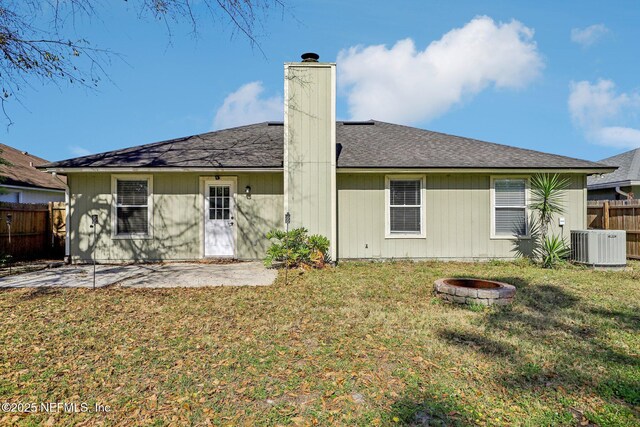 rear view of property featuring a patio, central air condition unit, a fire pit, and a lawn