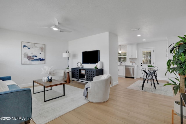 living room with ceiling fan, sink, light hardwood / wood-style floors, and a textured ceiling