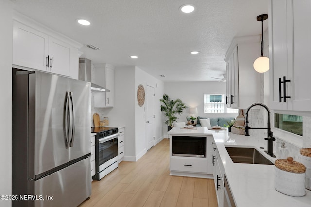 kitchen with electric range oven, pendant lighting, stainless steel refrigerator, sink, and wall chimney exhaust hood