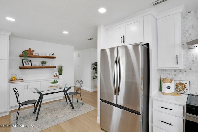 kitchen with stainless steel fridge, white cabinetry, backsplash, range with electric cooktop, and light wood-type flooring