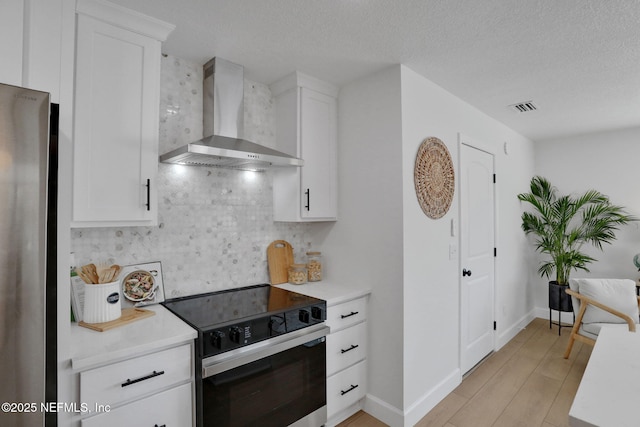 kitchen featuring range with electric cooktop, white cabinets, stainless steel fridge, and wall chimney range hood