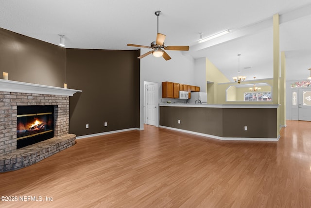 unfurnished living room featuring high vaulted ceiling, a fireplace, ceiling fan with notable chandelier, and light wood-type flooring