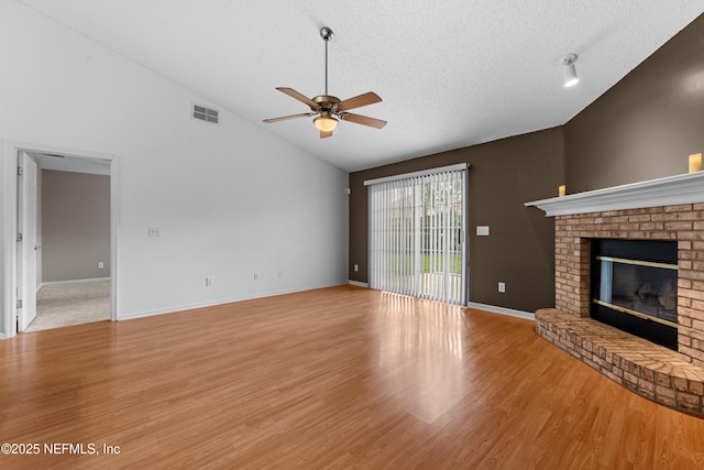 unfurnished living room with high vaulted ceiling, a textured ceiling, a brick fireplace, light wood-type flooring, and ceiling fan