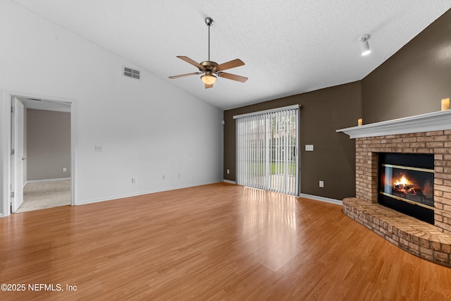 unfurnished living room featuring high vaulted ceiling, a fireplace, ceiling fan, a textured ceiling, and light wood-type flooring